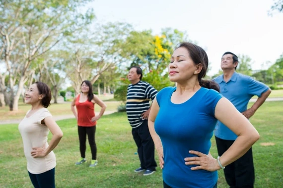 A group of people stand outdoors with hands on hips and eyes closed, focusing on rhythmic breathing.